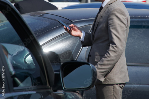 A man in a business suit - a driver or an emergency commissioner uses a smartphone at the scene of a traffic accident, near black cars. Problem solving and insurance