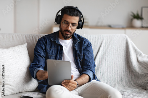 Indian guy spending time at home with digital tablet and wireless headphones photo