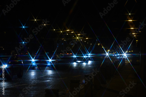 Night traffic jam on the road lit by lanterns in the form of stars. Many cars driving on a miserable night and black sky with star-shaped headlights on. Selective focus.