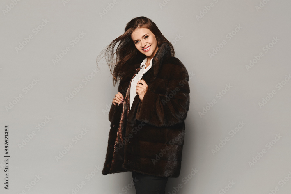 Model girl with shiny smile in a luxurious winter fur coat on the grey background, isolated. Winter fashion Model girl with shiny smile in a luxurious winter fur coat on the grey background, isolated. Winter fashion