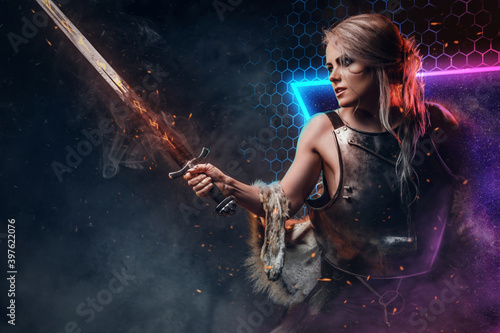 Dressed in heavy steel vest with fur female battle mage with burning sword in colourful abstract background.