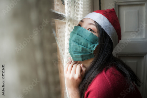 sad Christmas home alone during covid19 - young beautiful and depressed Asian Korean woman in Santa Claus hat and face mask looking melancholic and unhappy feeling lonely © TheVisualsYouNeed