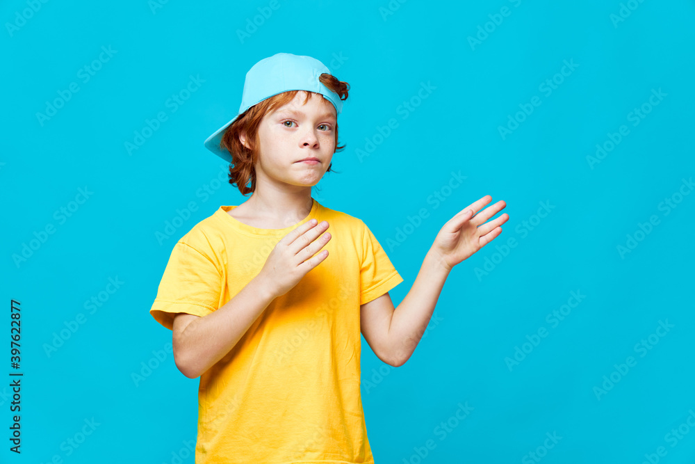 Red-haired boy gestures with his hands holding palms near him blue cap studio Red-haired boy gestures with his hands holding palms near him blue cap studio
