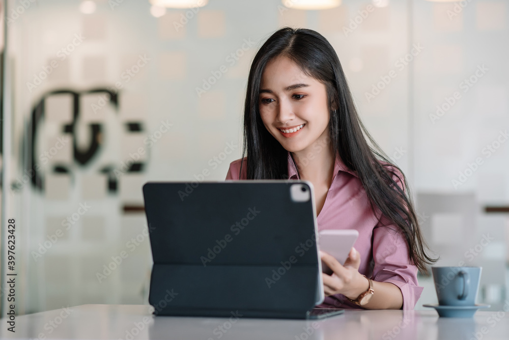 Young asian businesswoman beautiful charming smiling and using tablet and mobile phone, while sitting at table and working in office. Young asian businesswoman beautiful charming smiling and using tablet and mobile phone, while sitting at table and working in office.