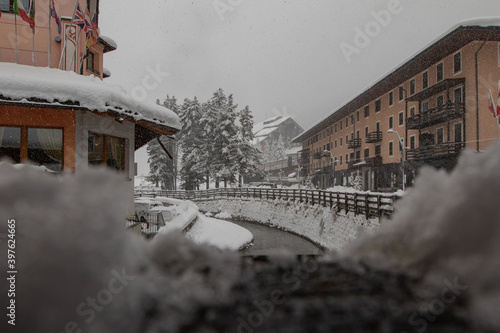 Small river Torrente Frigidolfo in the village of Santa Caterina in heavy snowfall. Visible hotels and houses with some snow flakes falling down. photo