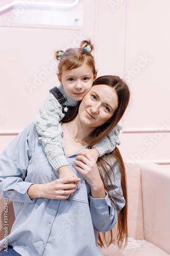 Happy loving family. young Mother and her little daughter are hugging and looking in camera on pink sofa and wall background. happy mother s  baby s day.