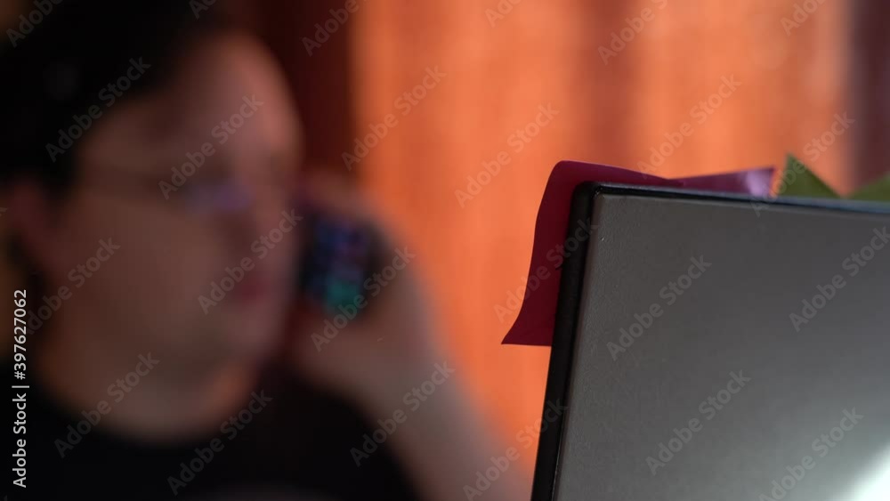 Young man busy with work talking on the phone in front of the monitor. Blurred background. Remote work at home. Young man busy with work talking on the phone in front of the monitor. Blurred background. Remote work at home.