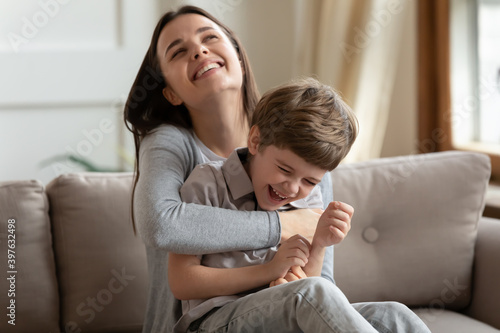 Overjoyed young Caucasian mom have fun playing with happy small preschooler son on weekend at home. Smiling mother or nanny involved in funny childish game activity, relax in living room together.