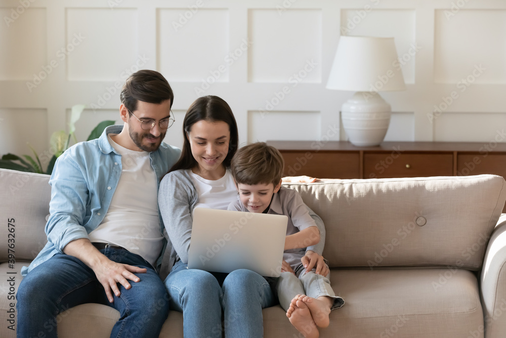 Young Caucasian family with little preschooler son relax on couch at home watch video on laptop together. Happy parents with small boy child use modern computer, rest on sofa in living room on weekend Young Caucasian family with little preschooler son relax on couch at home watch video on laptop together. Happy parents with small boy child use modern computer, rest on sofa in living room on weekend