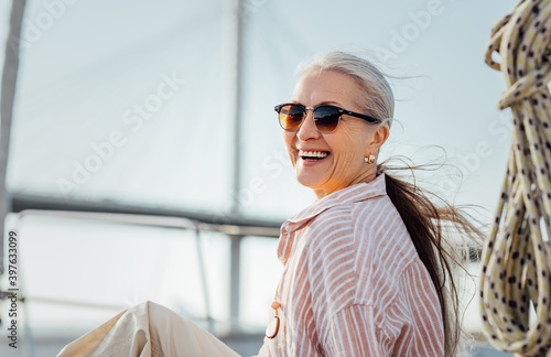 Laughing mature woman wearing sunglasses and looking at camera. Smiling female in casuals enjoying vacation. photo