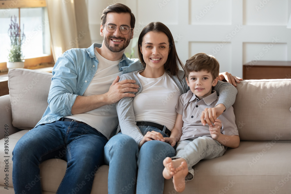 Portrait of happy young Caucasian family with little preschooler son sit relax on sofa in living room. Smiling parents mom and dad rest on couch at home, enjoy weekend together with small boy child. Portrait of happy young Caucasian family with little preschooler son sit relax on sofa in living room. Smiling parents mom and dad rest on couch at home, enjoy weekend together with small boy child.