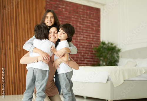 Love your kids. Happy latin children, teenage girl and two little twin boys hugging their mother while having fun together indoors. Mom playing with her children at home © Friends Stock