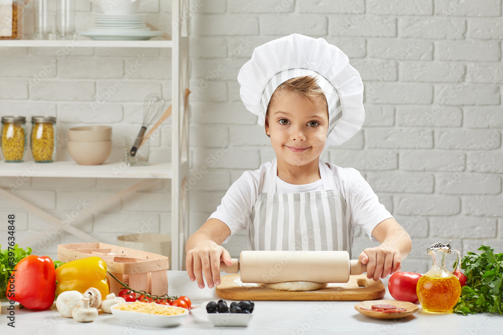 little child boy in chef hat and an apron rolled out the dough in the kitchen little child boy in chef hat and an apron rolled out the dough in the kitchen