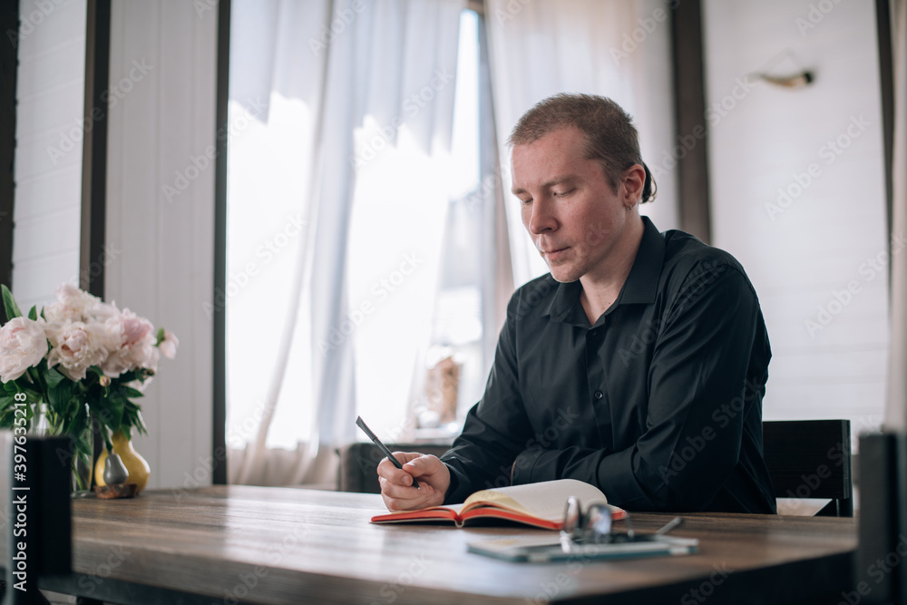 A young man writes in a notebook at the table A young man writes in a notebook at the table