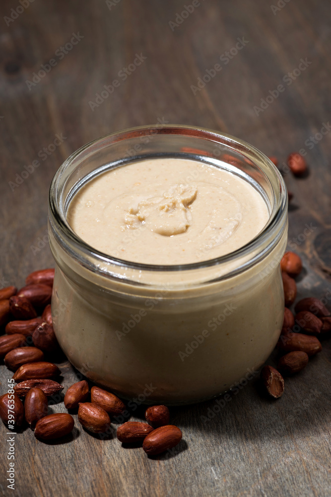 peanut butter in a glass jar on a wooden background, vertical closeup peanut butter in a glass jar on a wooden background, vertical closeup