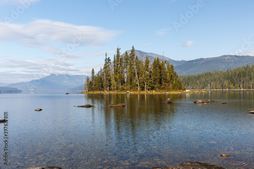 Evergreen forest on Emerald Island in Lake Wenatchee with mountain background and calm water.