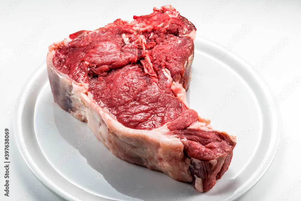 Raw T-bone steak on white round plate Raw T-bone steak on white round plate