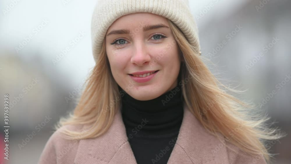 Close-up portrait of a young girl in a coat and hat stands on a city street. Enjoying fresh cold air on nature with smile Close-up portrait of a young girl in a coat and hat stands on a city street. Enjoying fresh cold air on nature with smile