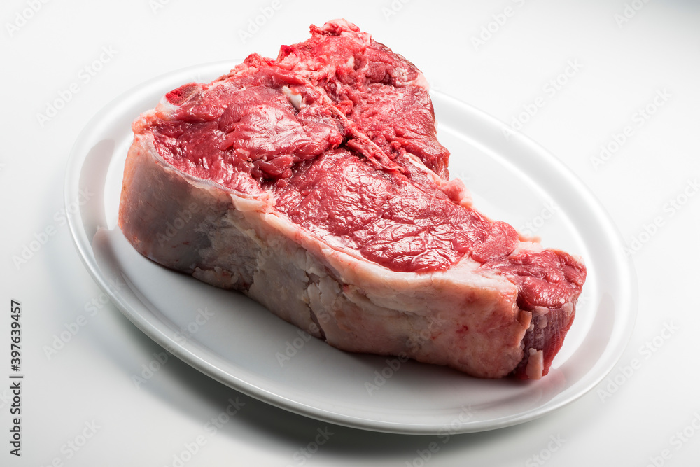 Raw T-bone steak on white round plate