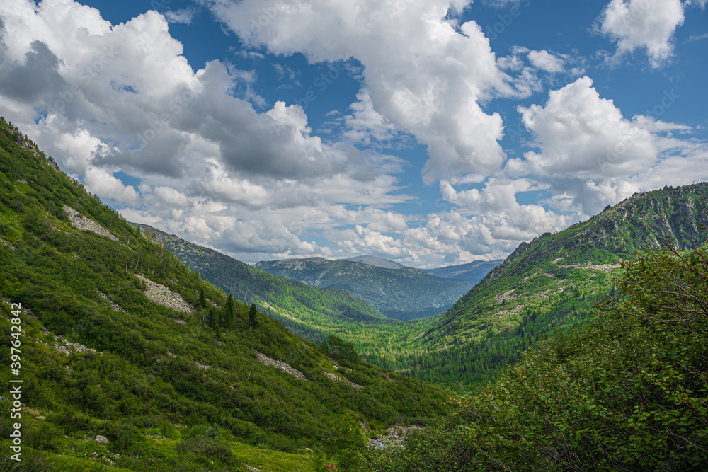 Panoramic view of rocky ridge. Mountains on horizon under cloudy sky. Travel through mountain valley on sunny day. Panoramic view of rocky ridge. Mountains on horizon under cloudy sky. Travel through mountain valley on sunny day.