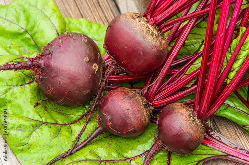 Beetroot tubers with green leaves on wooden table. Preparation of fresh salad. Fresh vegetables for vegetarian cooking. Beets on street market stall.