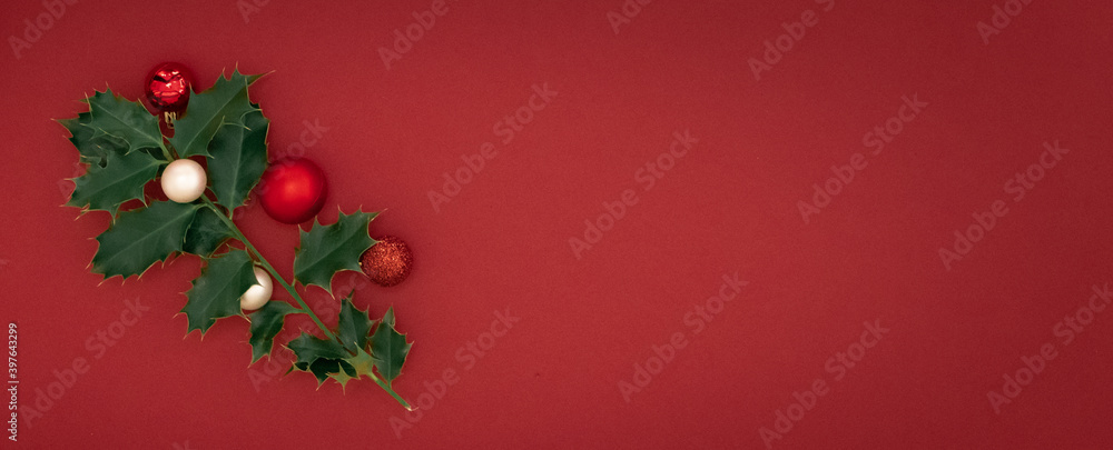 Christmas Composition Concept.  Green ilex brenches with red christmas balls on red background. Flat lay, top view.