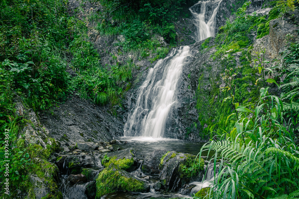 Atmospheric view of waterfall on river in rainforest. Swift stream among rocks and green moss. Atmospheric view of waterfall on river in rainforest. Swift stream among rocks and green moss.