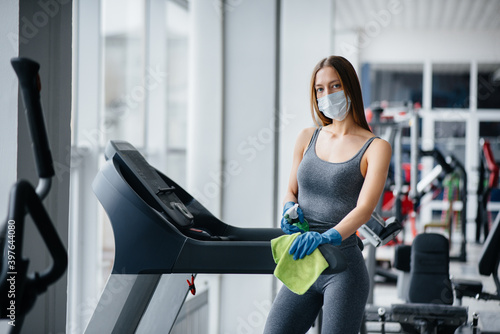 The girl in the mask disinfecting the gym equipment during a pandemic.