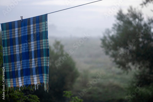 The peshtemal bath sheet hangs on a rope on a foggy morning on the river. Peshtemal with a checkered pattern dries on a rope in the morning. The hamam towel is attached to the rope with a clothespin photo