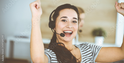 Business woman using headset for communication and consulting people at customer service office. Call center. Group of operators at work at the background. Casual dress style