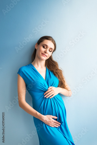 portrait of a dreaming pregnant woman in a blue dress on a blue background