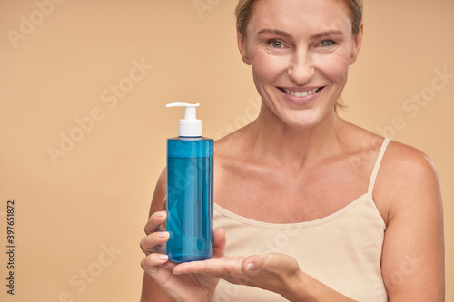 Smiling lady holding micellar water in bottle in studio