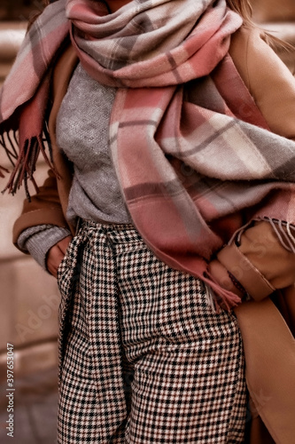 Young woman with cropped head in cozy scarf and brown coat walking on the street. Outdoor portrait in daylight. Warm winter clothes concept © asauriet