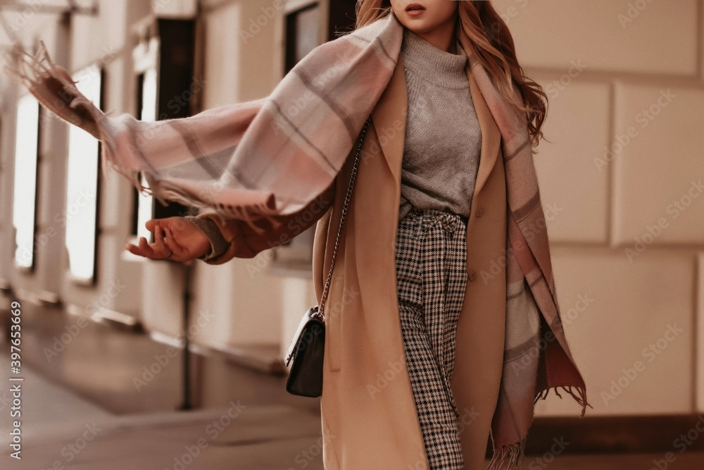 Young woman with cropped head in the grey knitted cozy sweater and brown coat walking on the street. Outdoor portrait in daylight. Warm winter clothes concept - obrazy, fototapety, plakaty 