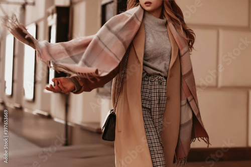 Young woman with cropped head in the grey knitted cozy sweater and brown coat walking on the street. Outdoor portrait in daylight. Warm winter clothes concept photo