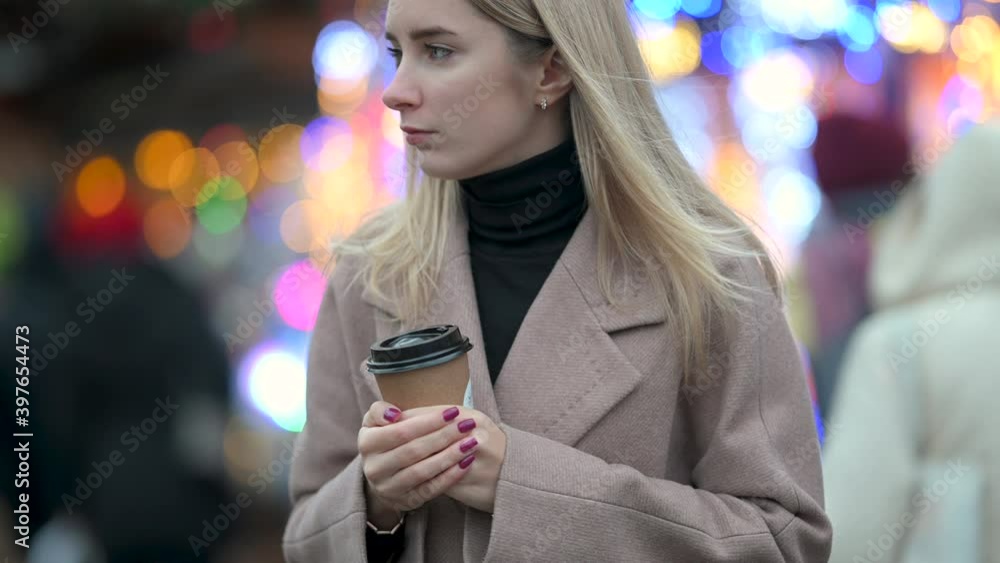 Young blonde girls with a cup of hot tea on the background of festive lights at the Christmas fair with the city. Holiday season. Merry christmas Young blonde girls with a cup of hot tea on the background of festive lights at the Christmas fair with the city. Holiday season. Merry christmas