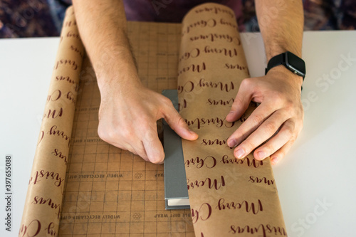 Photo of a man wrapping a book for a Christmas present. Nice wrap, gift, preparing for Christmas holidays, top view.