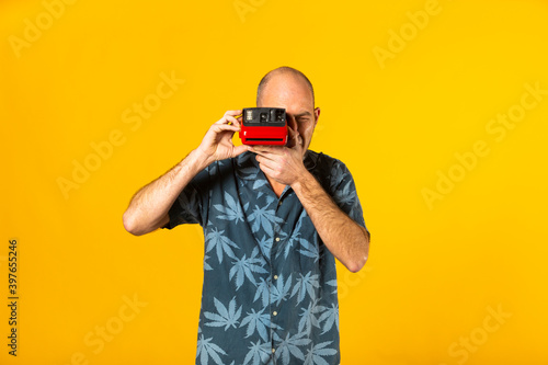 Adult man taking pictures with a red instant camera against a yellow background photo