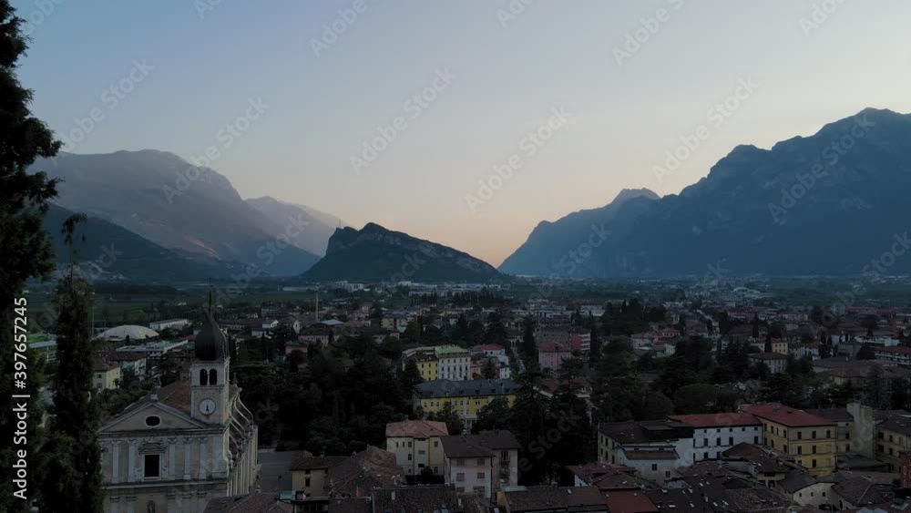 Aerial shot revealing Riva del Garda, Trentino, Italy, at sunrise or sunset. Drone passes through tress and reveals the city. Countryside concept Aerial shot revealing Riva del Garda, Trentino, Italy, at sunrise or sunset. Drone passes through tress and reveals the city. Countryside concept