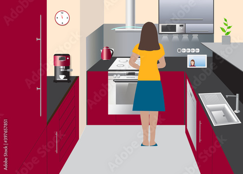 Woman is cooking and communicating online via tablet in the U shaped red color kitchen