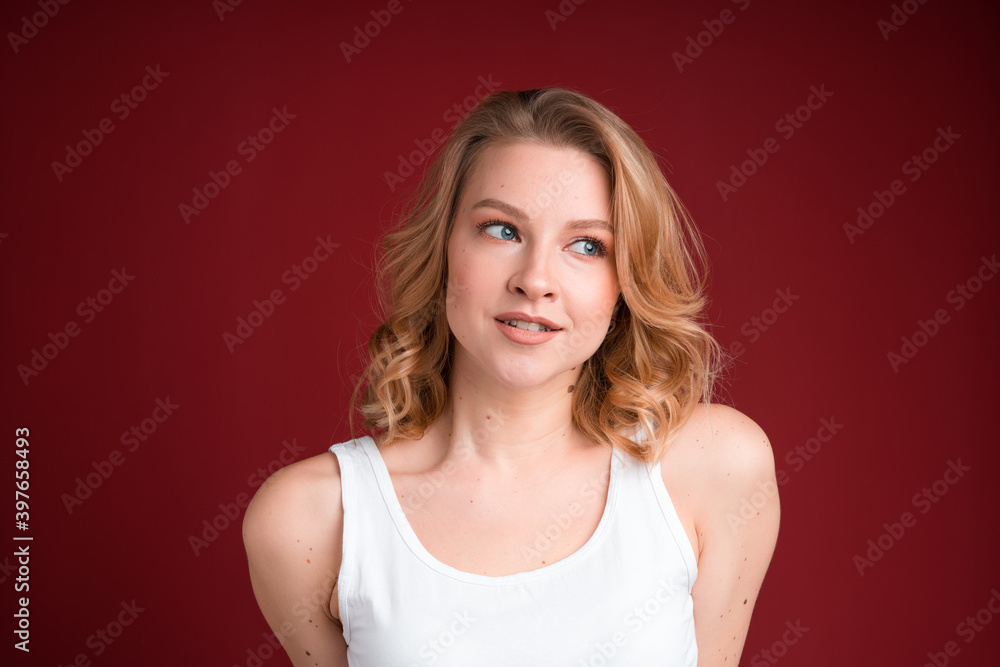 Shy blond woman with curly hair in white tank top on the red background. Shy blond woman with curly hair in white tank top on the red background.