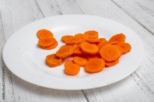 Sliced carrots on a plate. On a white wooden background.