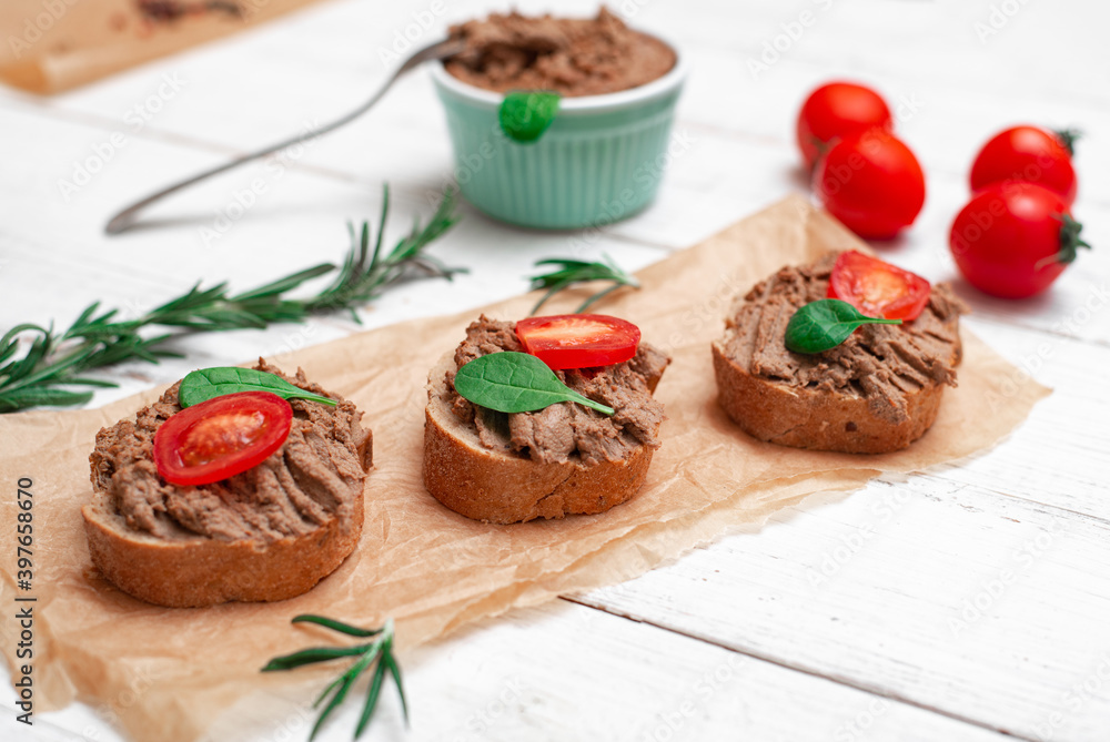 Chicken liver pate. Sandwiches, canapes with pate with cherry tomatoes on a white wooden background.