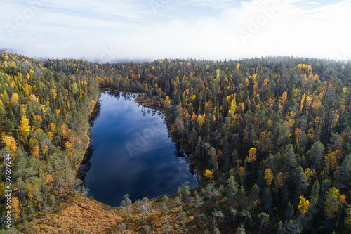 An aerial view of a small lake in the middle of colorful Finnish taiga forest.