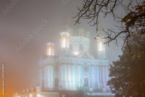 The ancient Baroque St. Andrew's Church rises above Andriyivskyy Uzviz and Vozdvyzhenka in a thick autumn fog. Mysterious and charming plot from the narrow streets of the ancient city of Kyiv, Ukraine photo