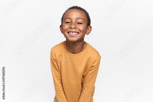 Positive emotions, joy and happy childhood. Adorable black boy posing against blank white copy space studio wall background, looking at camera with broad cheerful smile, anticipating holidays