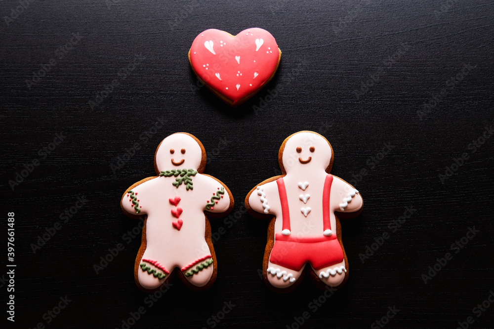 Gay love. Valentine Day. Conceptual background. Homosexual romantic relationship. Happy gingerbread man couple with red heart creative cute composition on black wooden texture copy space.