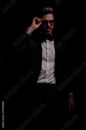 cool unshaved guy in black velvet tuxedo fixing glasses