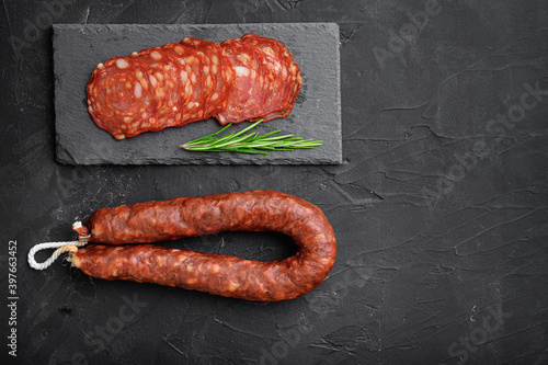 Whole and sliced chorizo sausage on black textured surface with space for text
