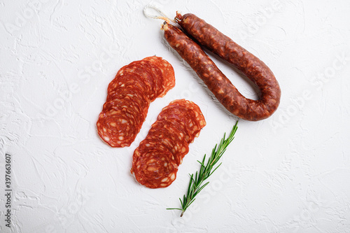 Sliced cuts of chorizo salami sausage on white textured background, topview
